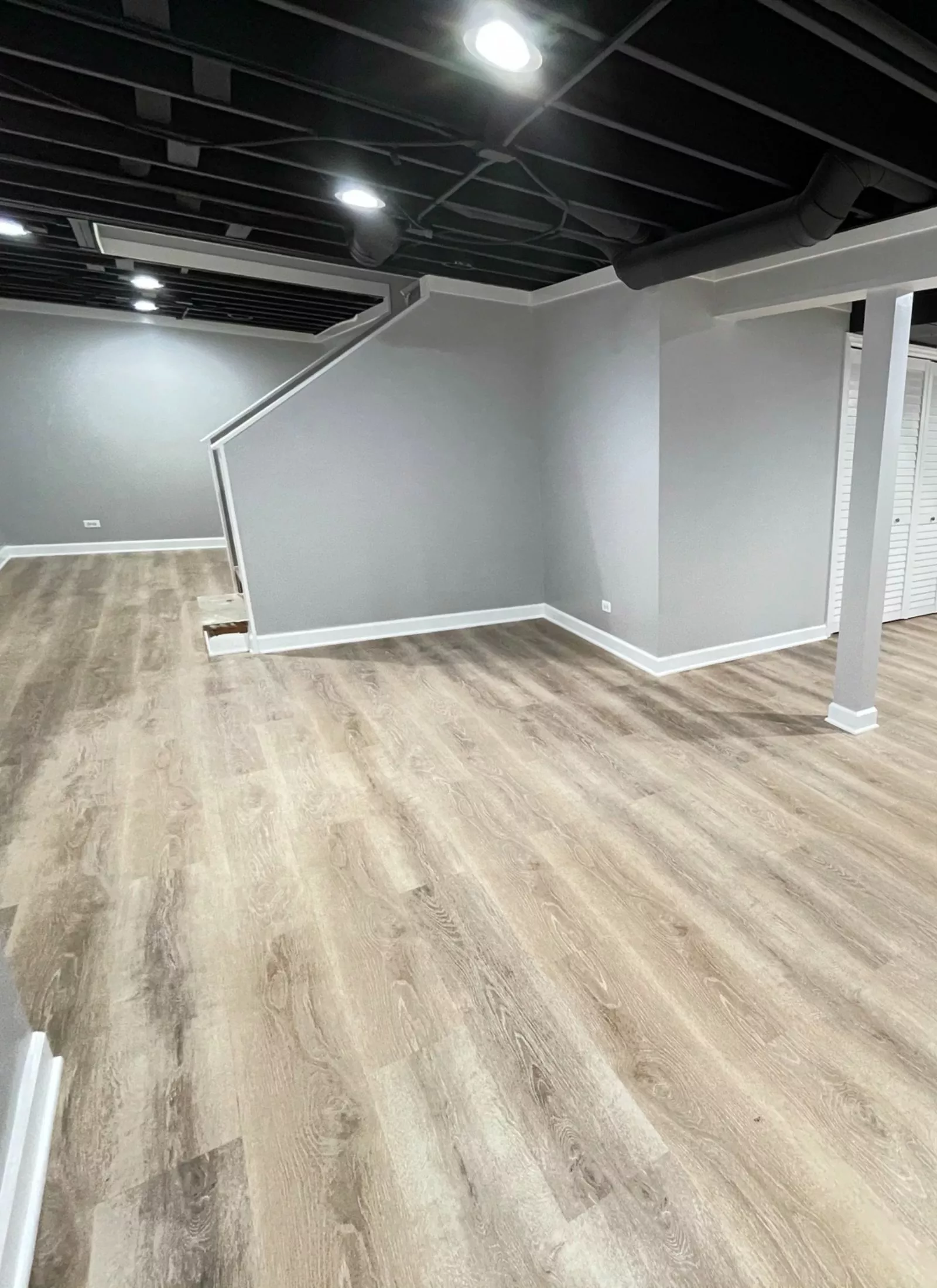 A basement with wood floors and white walls undergoing a bathroom renovation.