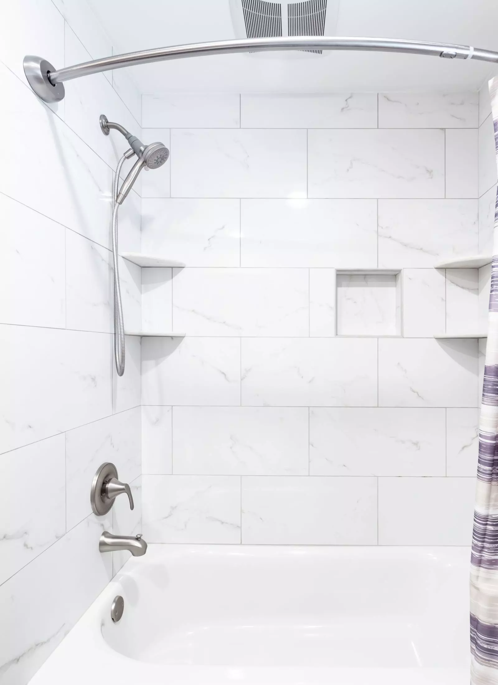 A white tiled bathroom with a purple shower curtain.