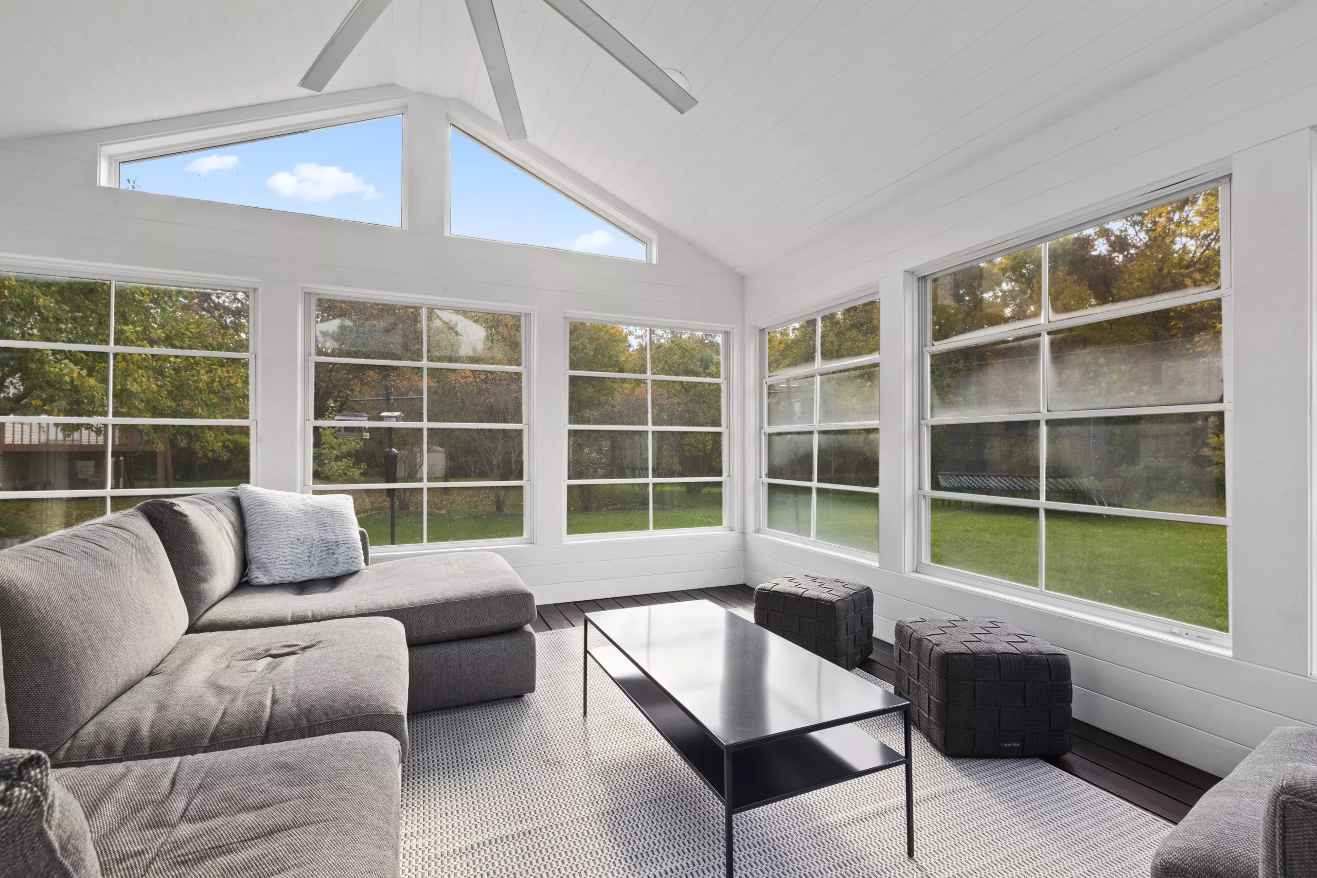 A sunroom with large windows and a gray couch perfect for relaxation and enjoying the natural daylight.