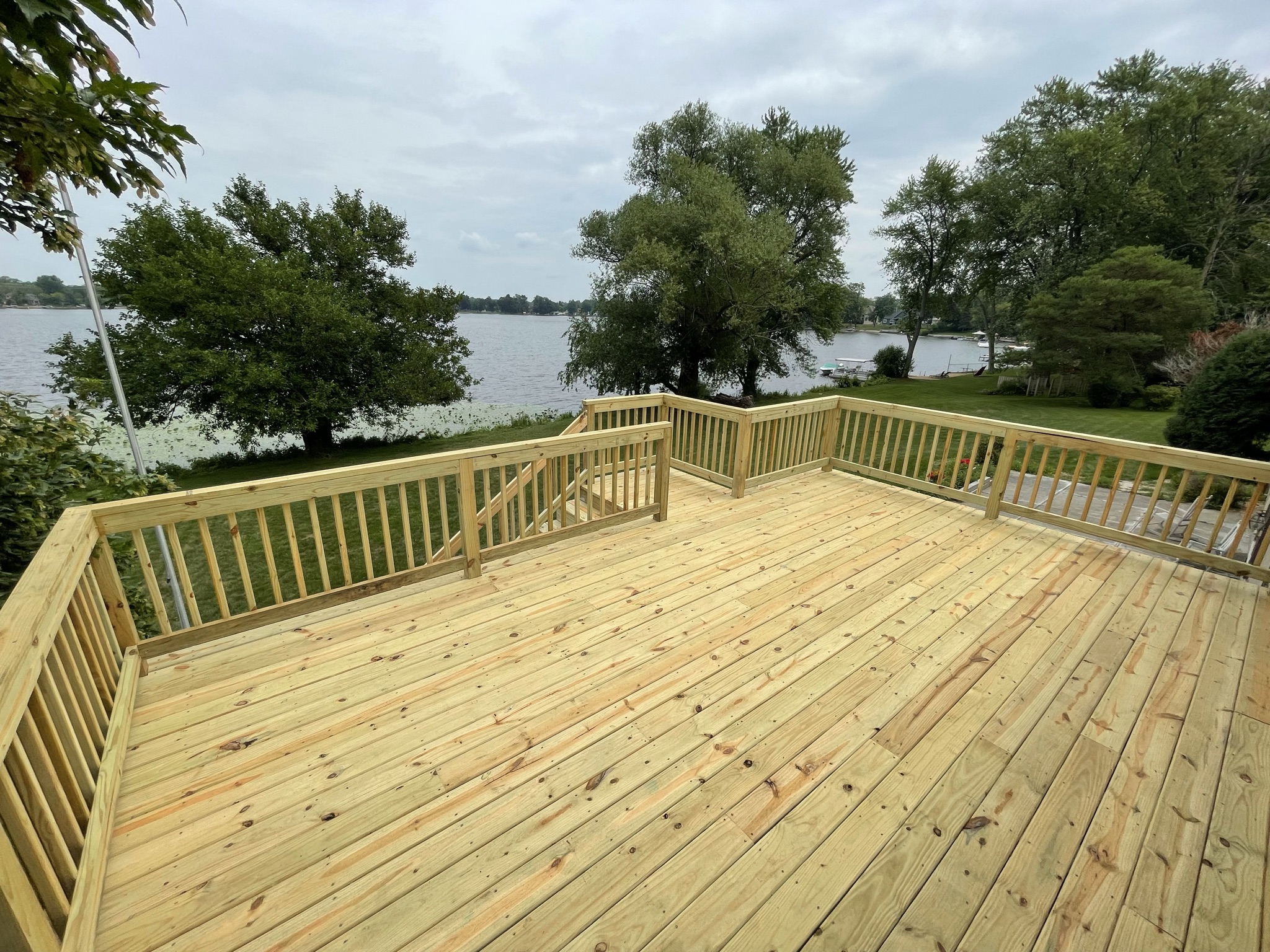 A new wooden decking boards overlooking a tranquil lake with lush greenery on the banks.